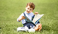 smiling young boy sitting outside with an open book in his hands